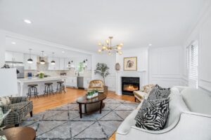 Open-concept living room and kitchen with modern white cabinetry, pendant lighting, fireplace, and elegant furnishings.